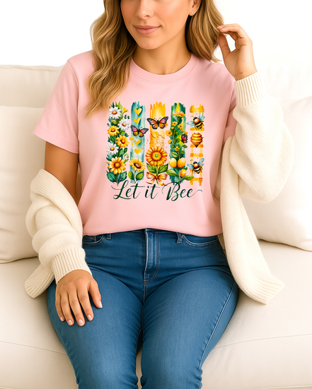 Woman wearing a pink t-shirt with a colorful 'Let it Bee' design, sitting on a white couch.