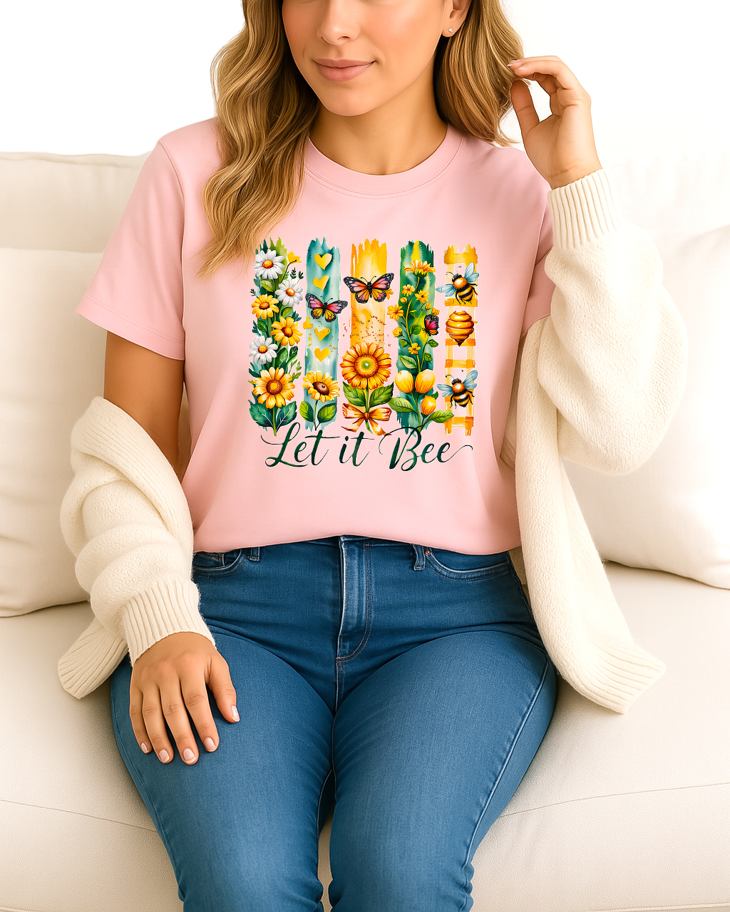 Woman wearing a pink t-shirt with a colorful 'Let it Bee' design, sitting on a white couch.