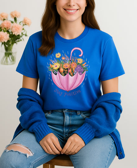Woman wearing Blue Stay Positive T-shirt with pink umbrella floral design, handmade organic cotton uplifting fashion tee