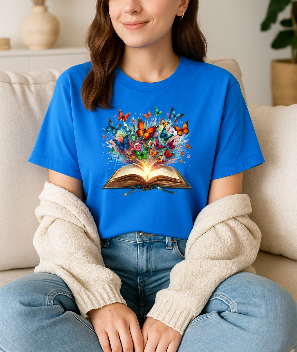 Person wearing a blue t-shirt with a colorful book and butterfly design, sitting on a couch.