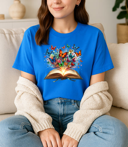 Person wearing a blue t-shirt with a colorful book and butterfly design, sitting on a couch.