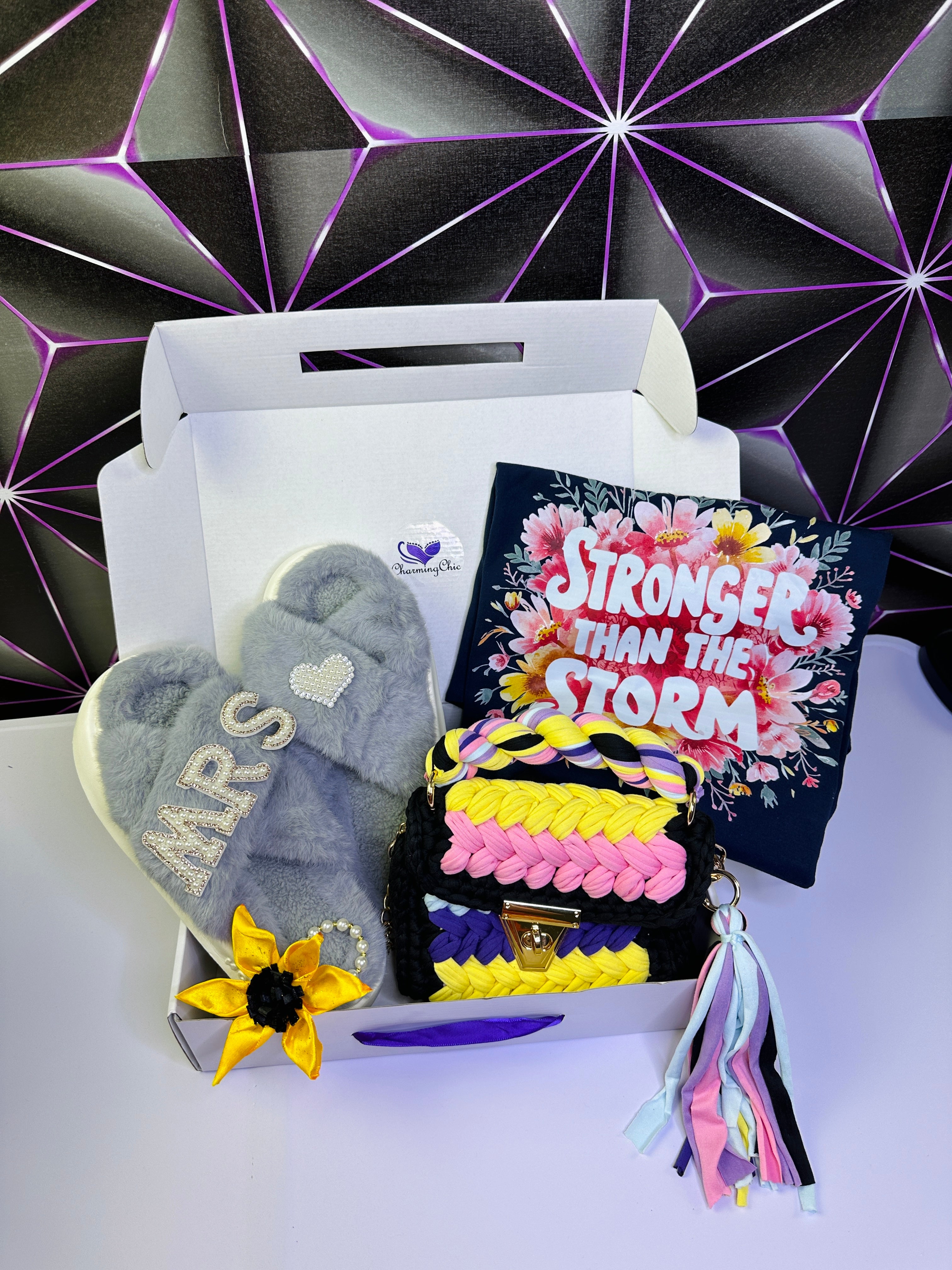 Box with gray fluffy slipper, colorful bag, and 'Stronger Than the Storm' book against a geometric patterned background.