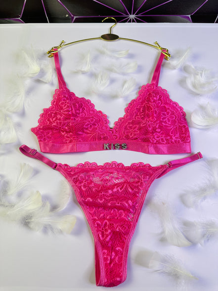 Pink lace lingerie set with 'Kiss' branding on a white surface.