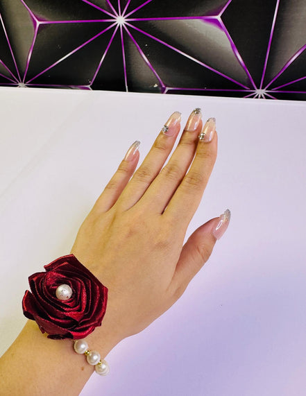 Hand wearing a red wrist corsage with pearls against a white background