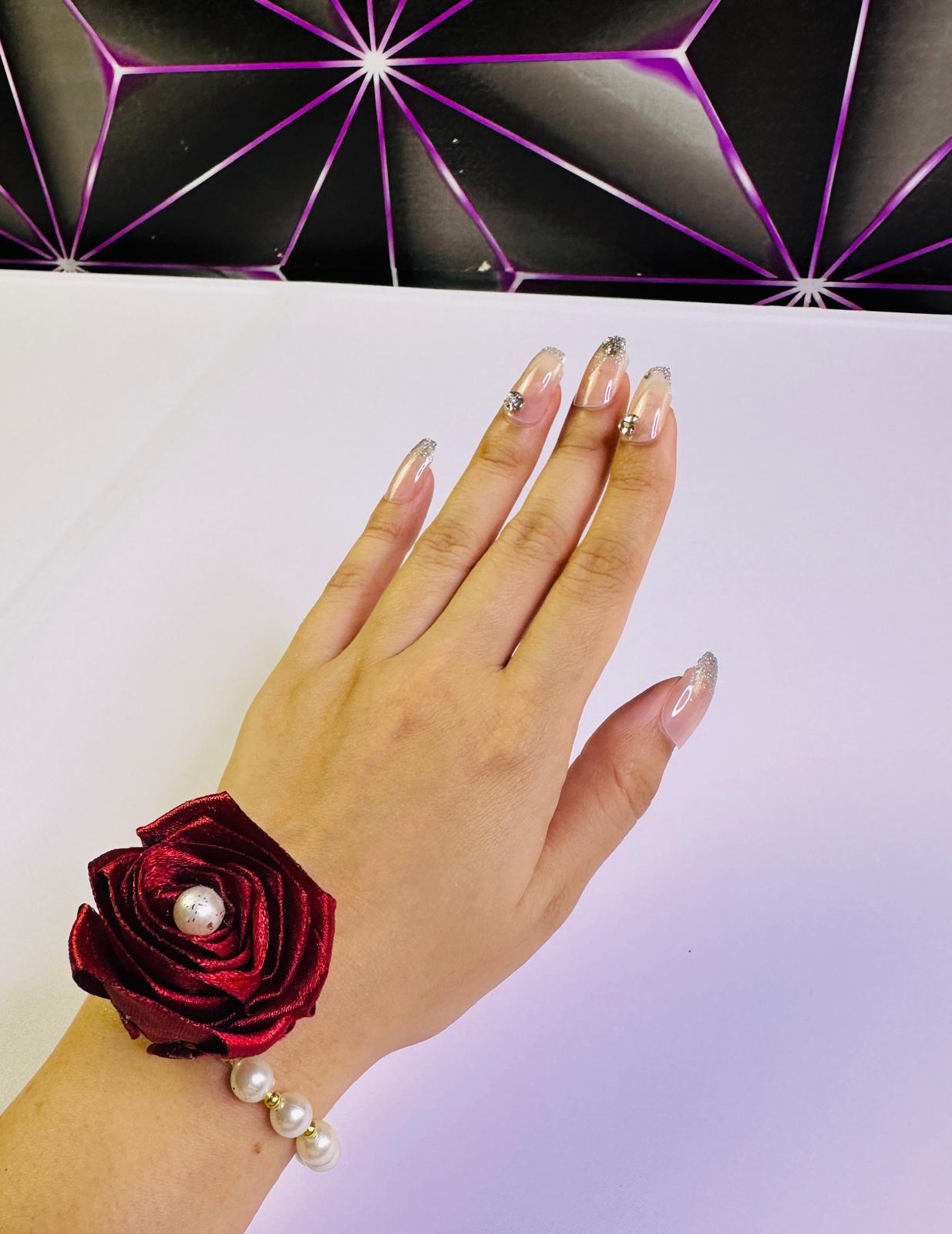 Hand wearing a red wrist corsage with pearls against a white background