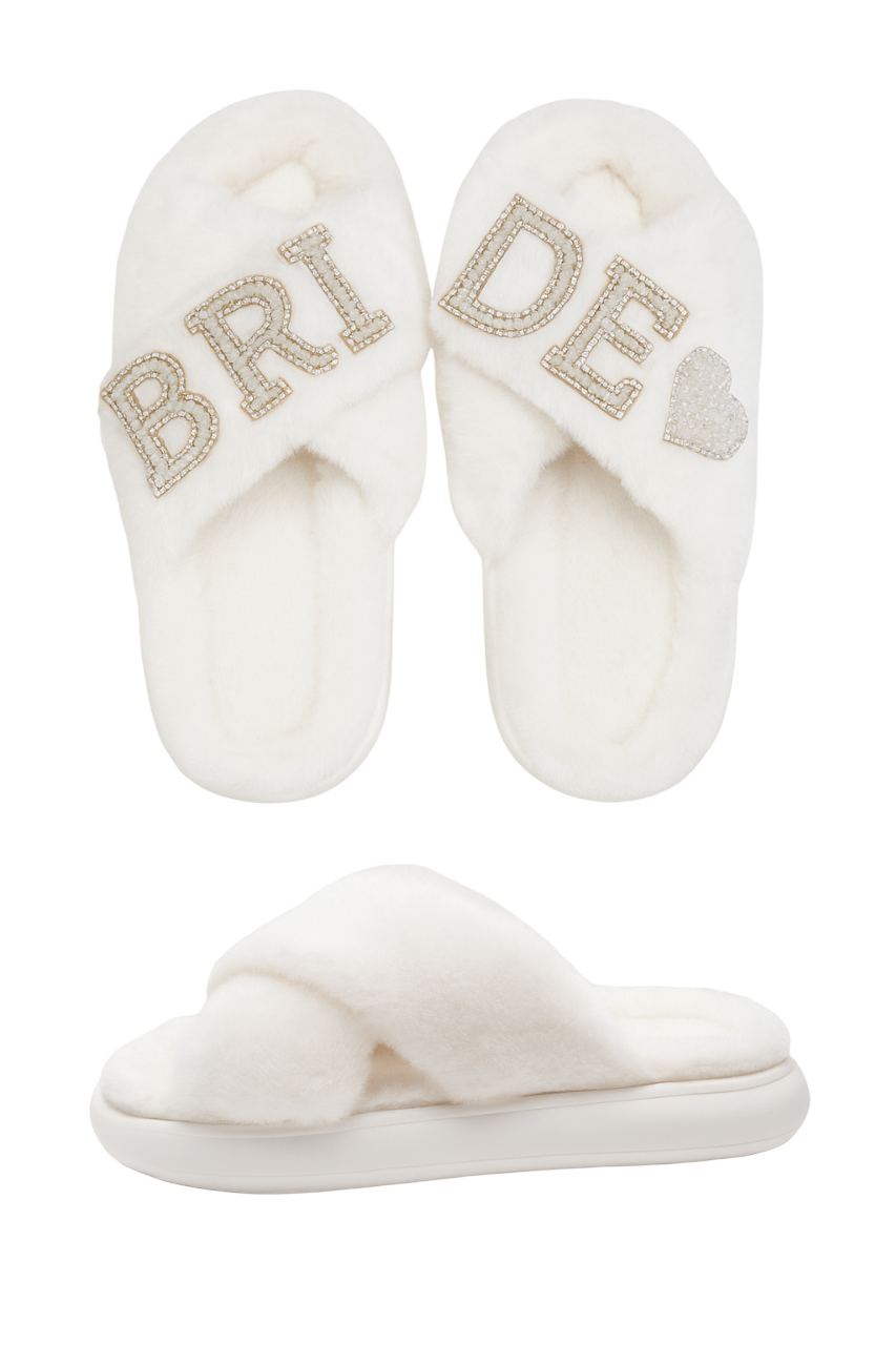 Pair of white slippers with 'Bride' and heart designs on a white background